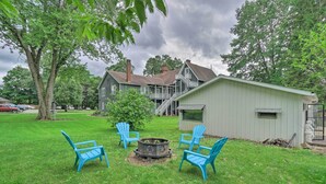 Un jardin avec un foyer, quatre chaises Adirondack bleues et un abri de jardin.