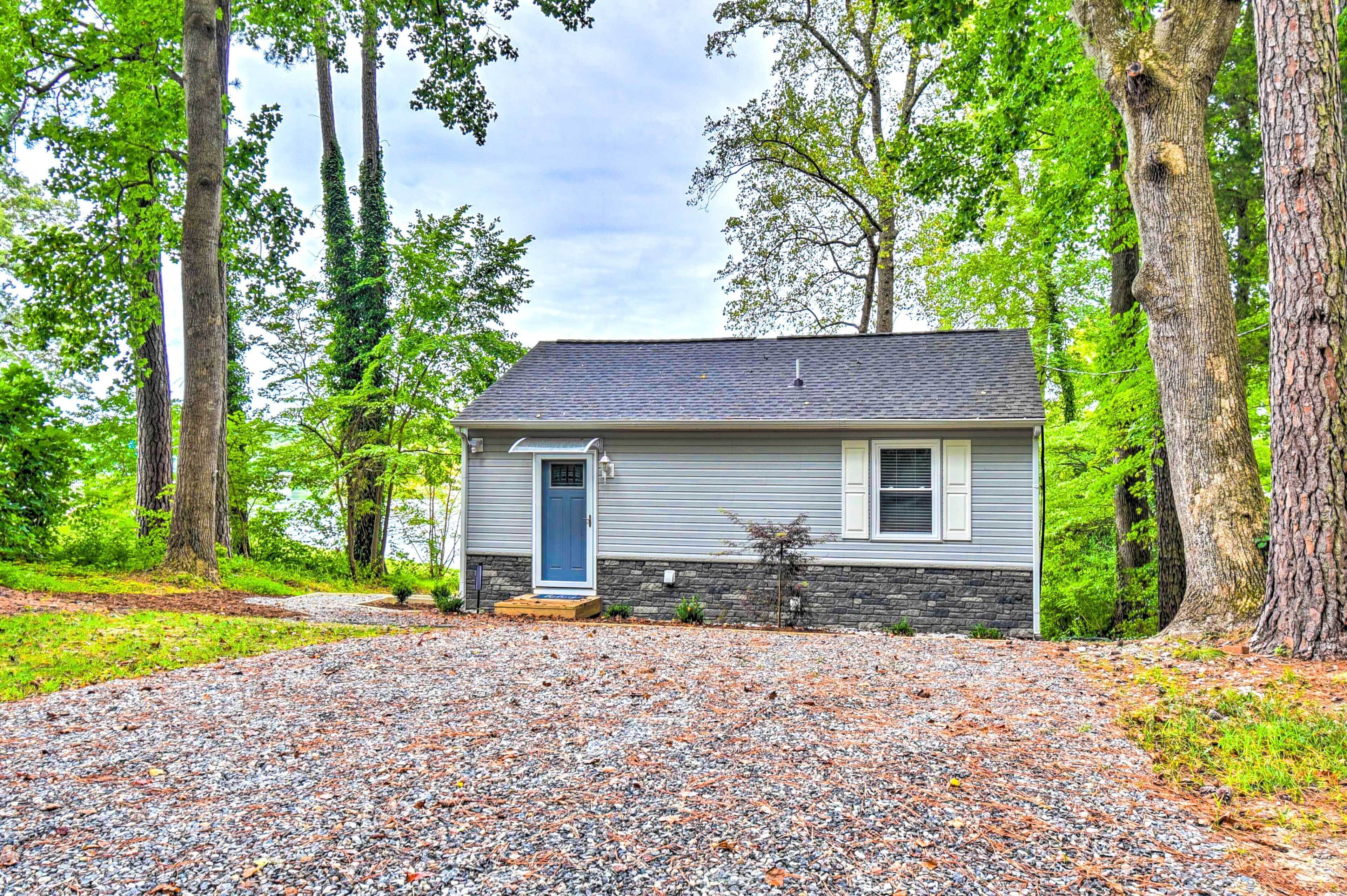 A small house with a blue door, surrounded by trees and a gravel driveway.