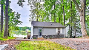 A single-story house with a stone foundation, a front porch, and a view of a lake. - Relaxing Riverfront Cottage w/ Boat Dock! (Gloucester)
