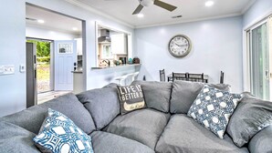 A modern living room with a gray sectional sofa, a ceiling fan, a dining area with a table and chairs, and a kitchen in the background. - Relaxing Riverfront Cottage w/ Boat Dock! (Gloucester)