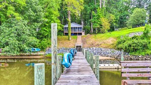 A wooden pier leading to a house surrounded by lush greenery. - Relaxing Riverfront Cottage w/ Boat Dock! (Gloucester)