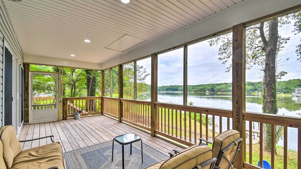A covered deck with outdoor seating, a view of a lake, and a wooden railing. - Relaxing Riverfront Cottage w/ Boat Dock! (Gloucester)