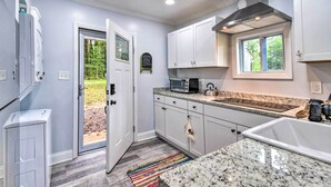 A modern kitchen with white cabinets, a granite countertop, a built-in microwave, and a window overlooking a garden. - Relaxing Riverfront Cottage w/ Boat Dock! (Gloucester)