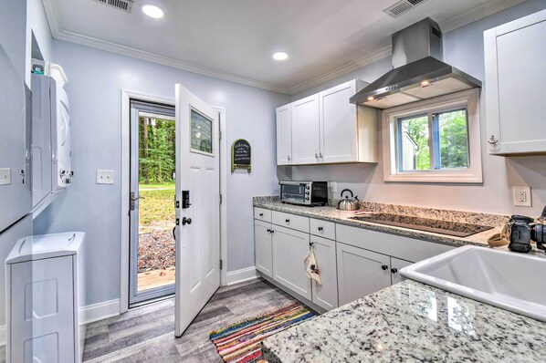 A modern kitchen with white cabinets, granite countertops, a built-in microwave, and a window overlooking a garden. - Relaxing Riverfront Cottage w/ Boat Dock! (Gloucester)