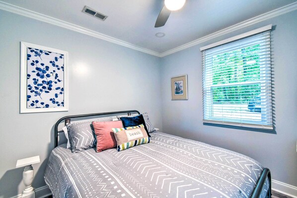 A bedroom with a bed, a nightstand, a framed picture, and a window with blinds. - Relaxing Riverfront Cottage w/ Boat Dock! (Gloucester)