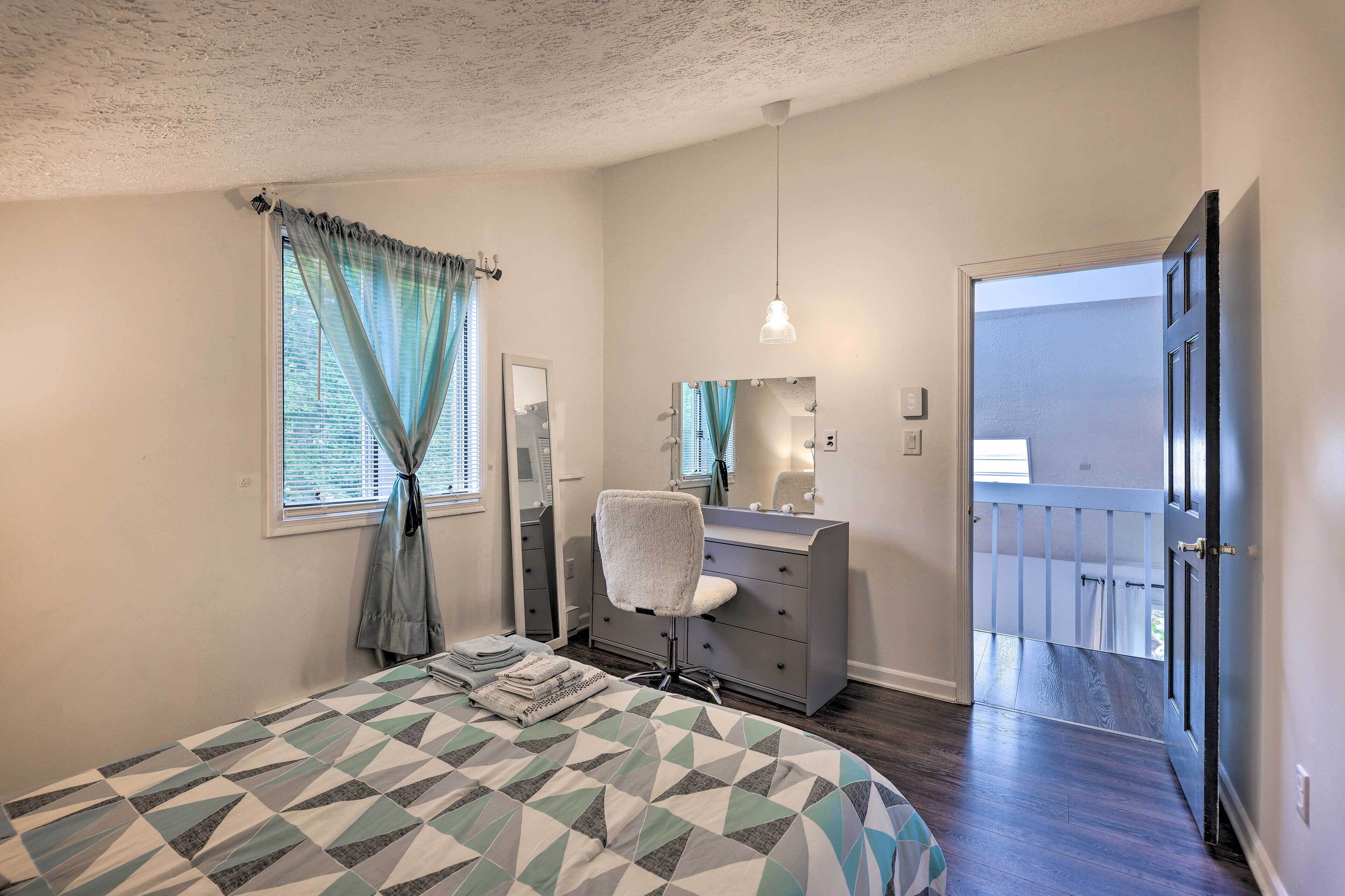 A bedroom with a bed, a dresser, a chair, a mirror, and a door leading to a balcony.