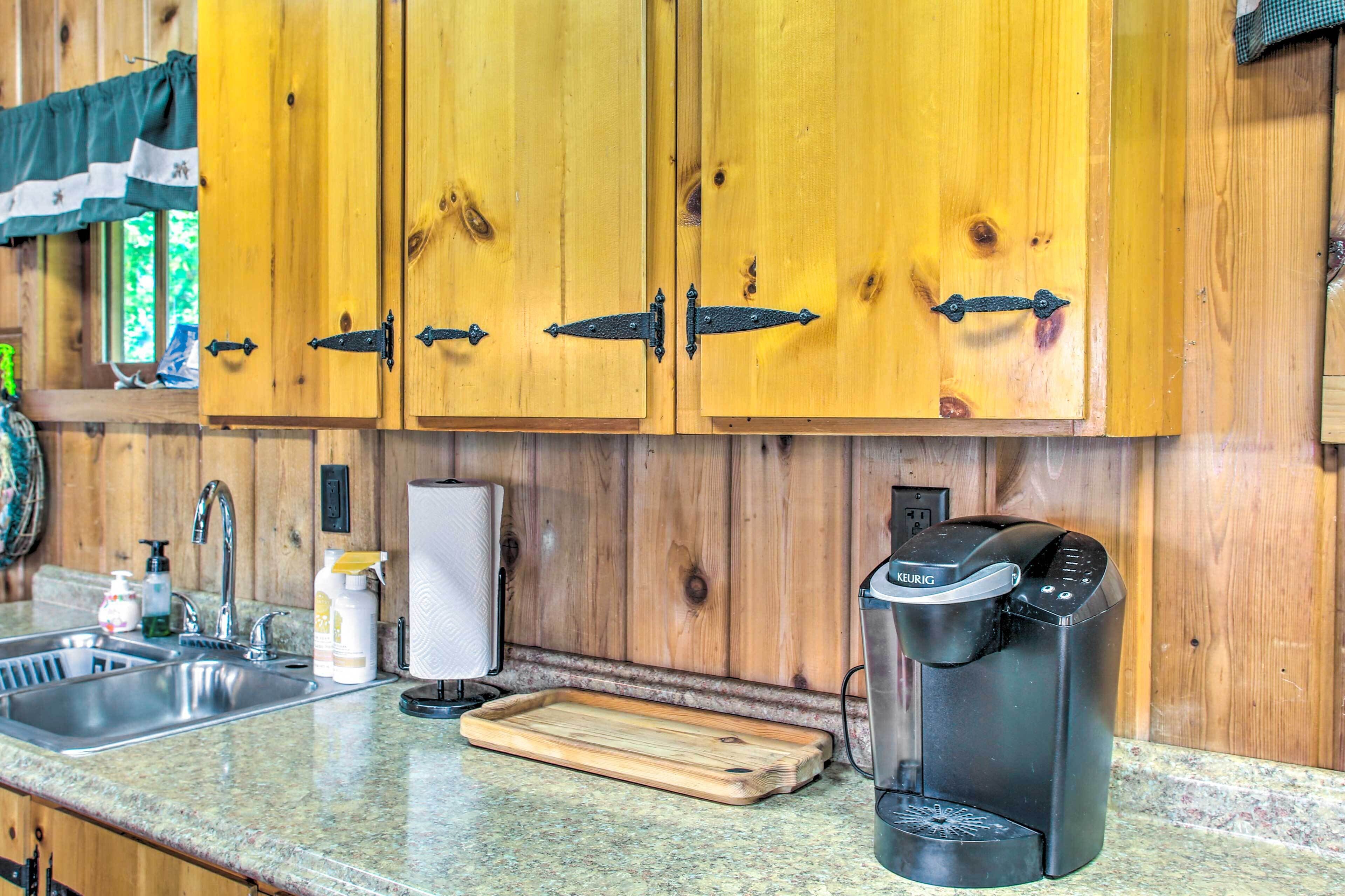 A kitchen with wooden cabinets, a coffee maker, a sink, and a cutting board.