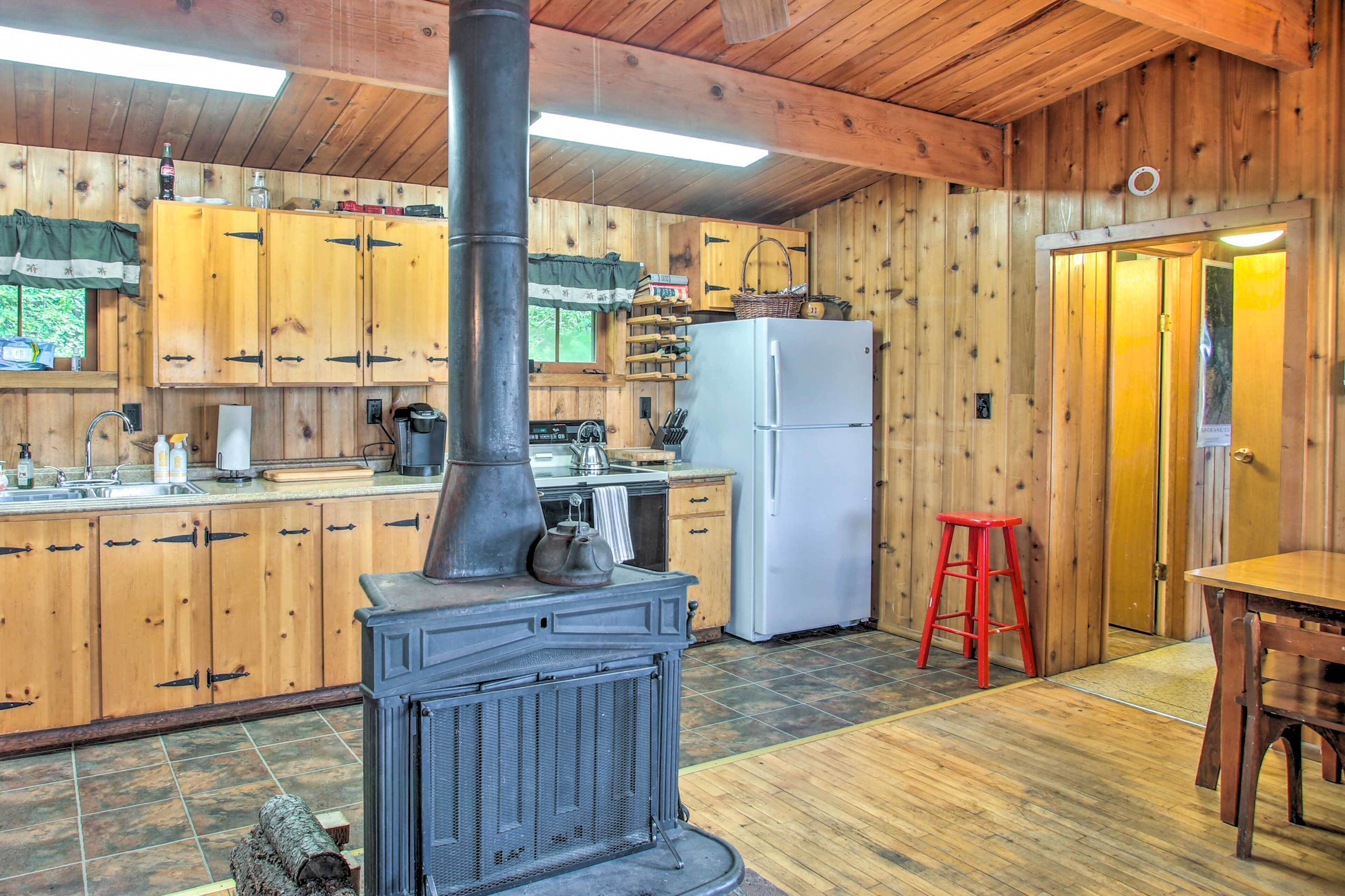 A wooden cabin kitchen with a central wood stove, cabinets, a refrigerator, and a dining area.