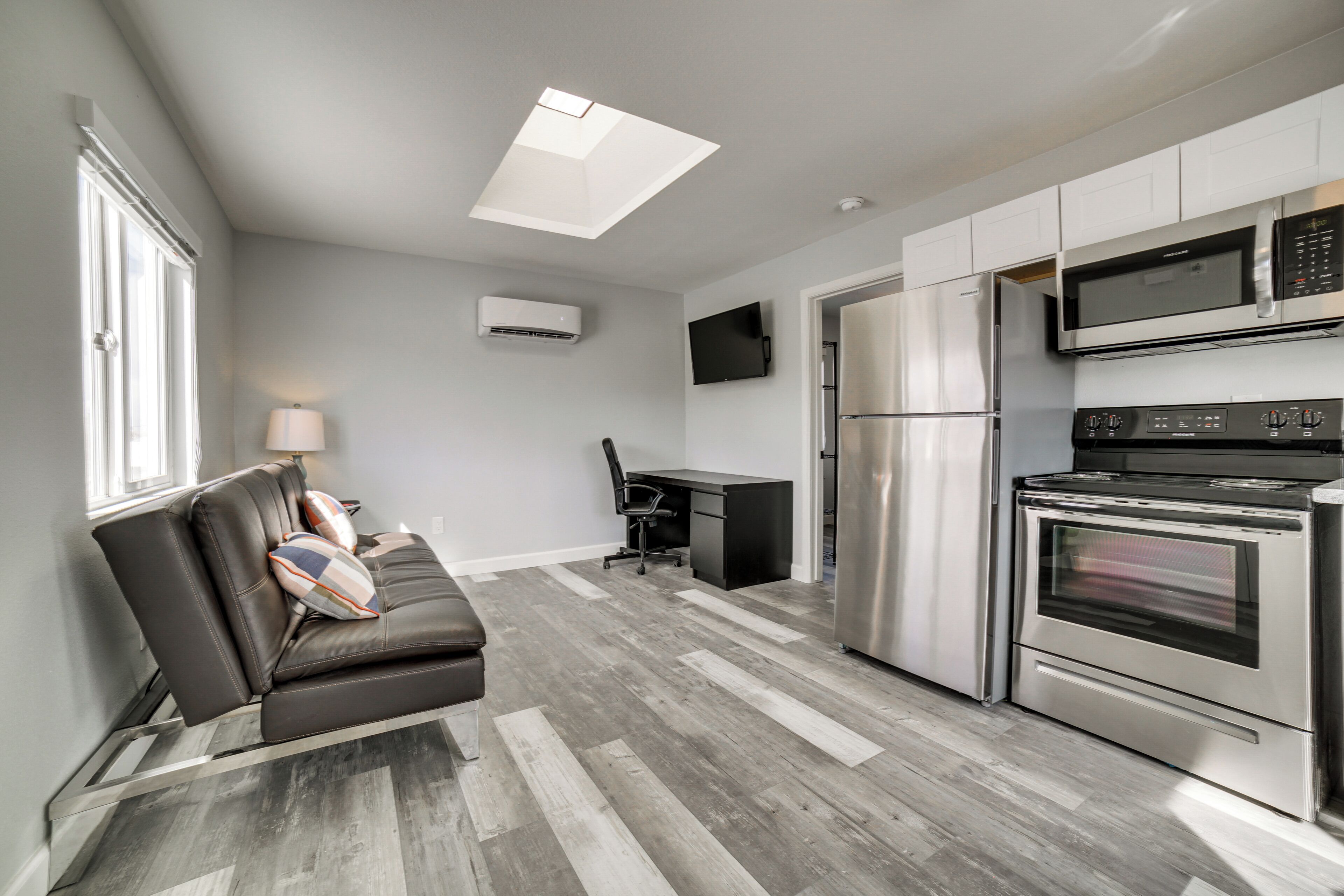 A modern kitchen with stainless steel appliances, a dining area with a table and chairs, and a sofa with cushions.