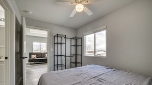 Ein Schlafzimmer mit einem Bett, einem Deckenventilator, einem Fenster und einer Tür zu einem anderen Raum.