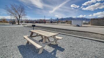 Una mesa de picnic en un área de grava, cielo despejado y montañas al fondo.