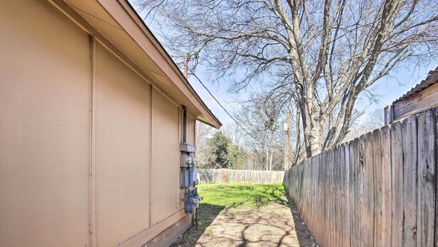 A narrow pathway between a beige building and a wooden fence, with a tree in the background. - San Antonio Abode w/ Yard: 17 Mi to Downtown! (San Antonio)