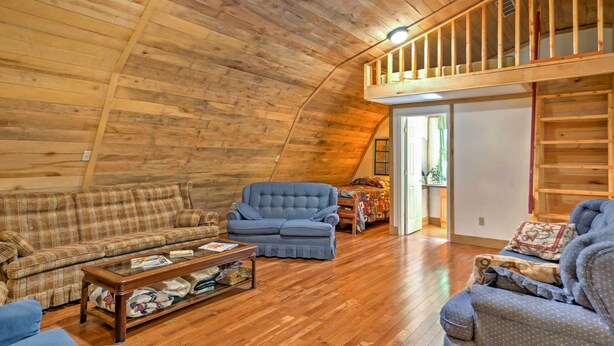 A cozy loft-style living room with wooden floors, a blue sofa, a matching armchair, and a wooden coffee table. - Rustic Taswell Cabin: Grill + Walk to Patoka Lake! (Taswell)