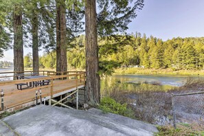 A wooden deck with picnic tables overlooking a calm lake, surrounded by tall trees. - Riverfront Crescent City Home, 8 Mi to Beach! (Crescent City)