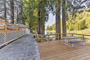 A wooden deck with picnic tables overlooking a river, surrounded by tall trees. - Riverfront Crescent City Home, 8 Mi to Beach! (Crescent City)