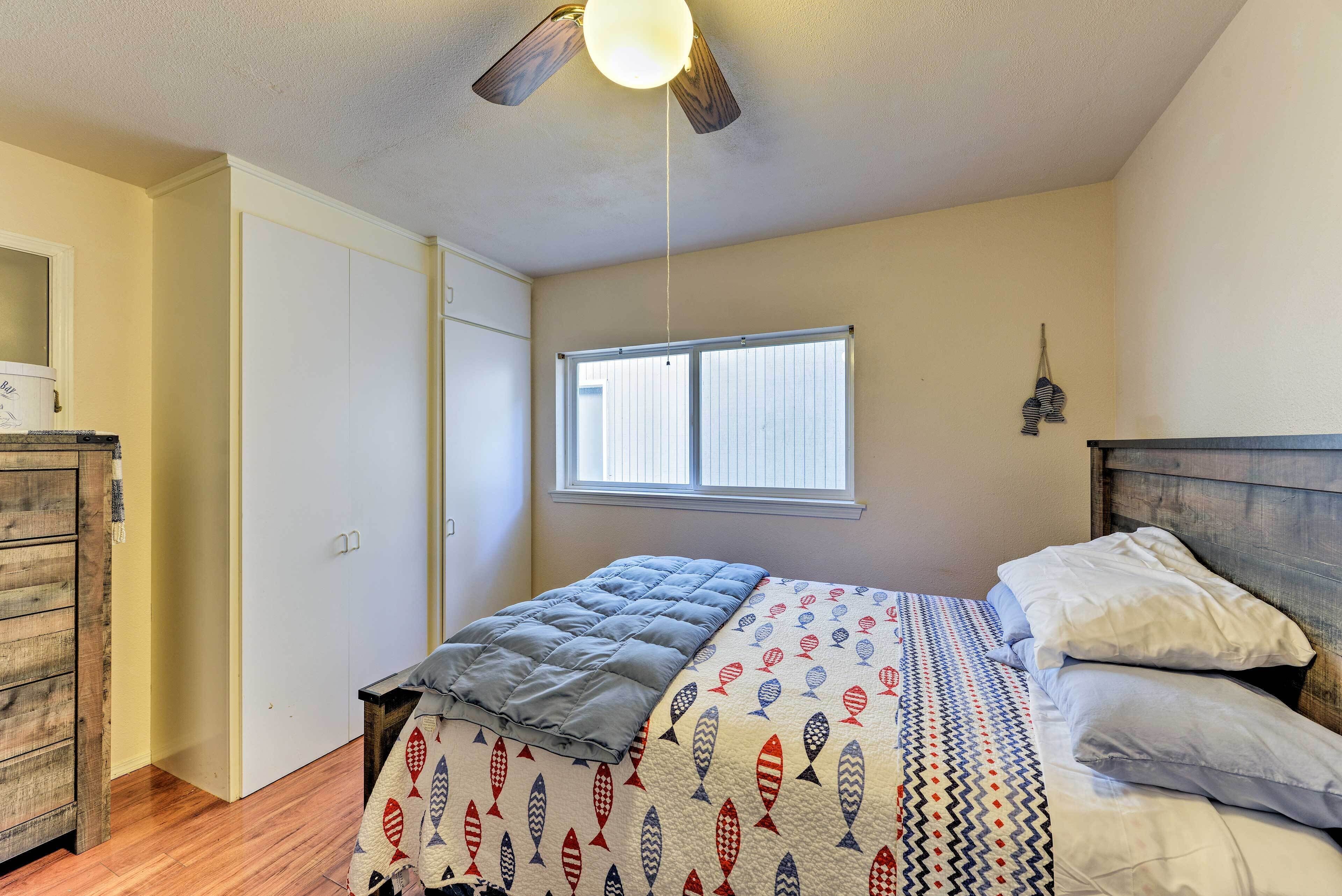 A bedroom with a bed, a ceiling fan, a window, and a wooden dresser.