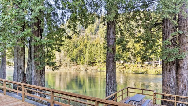 Un pontile in legno con panche che si affaccia su un lago calmo, circondato da alberi alti.