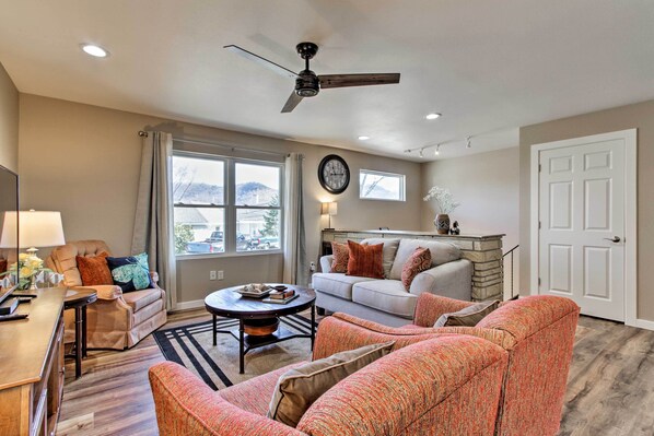 A spacious living room with a ceiling fan, a sofa, a coffee table, and a dining area with a lamp. - 'riversong' Waterfront La Crosse Home w/ Dock (La Crosse)