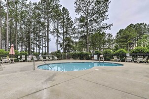 Piscina com espreguiçadeiras e guarda-sóis, rodeada por árvores altas.