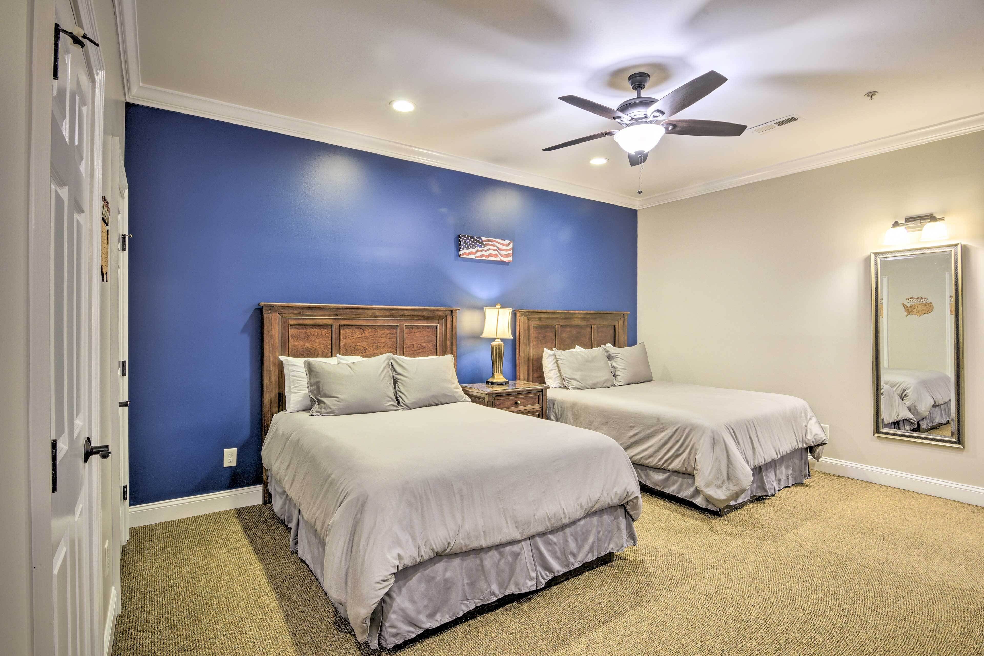 A hotel room with two beds, a ceiling fan, a nightstand with a lamp, and a mirror on the wall.