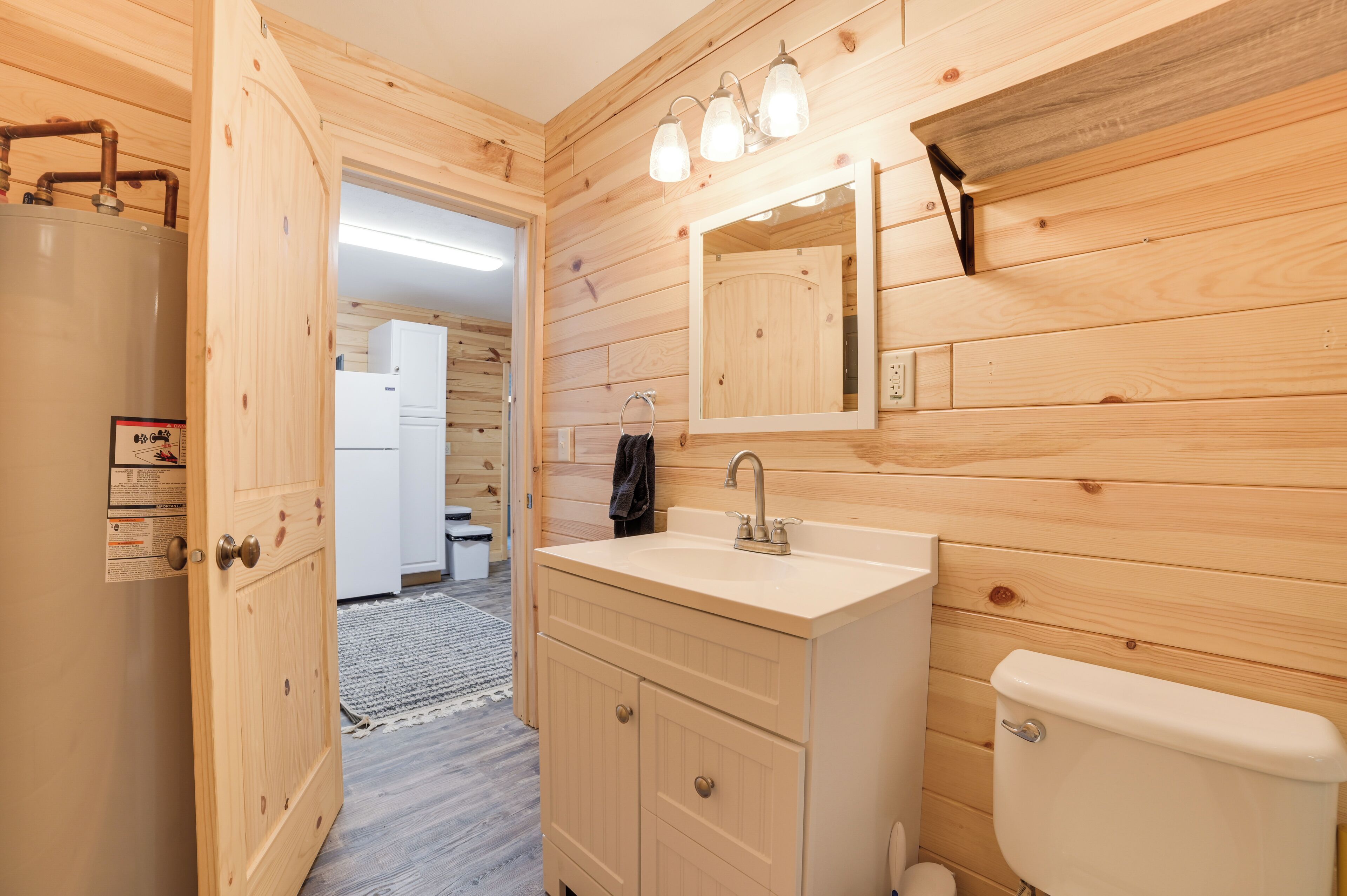Ein Badezimmer mit Holzwandverkleidung, Waschbecken, Spiegel und Toilette.