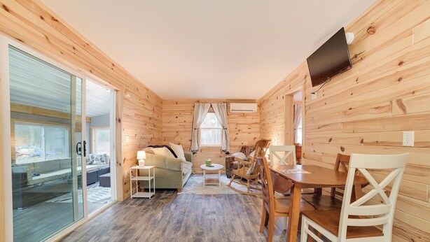 L’intérieur chaleureux d’un chalet, avec un décor en bois, un canapé, une table à manger et un téléviseur fixé au mur.