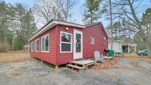 Une petite cabane rouge avec un porche à l’avant, une table de pique-nique et une chaise verte.