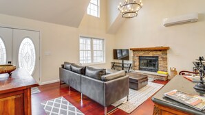 A spacious living room with a fireplace, a large sofa, and a dining area with a wooden table. - Large Deck & Fire Pit: Secluded Pocono Lake Home (Pocono Lake)