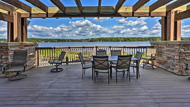 A wooden deck with a table and chairs, overlooking a body of water and a green landscape. - Large Deck & Fire Pit: Secluded Pocono Lake Home (Pocono Lake)