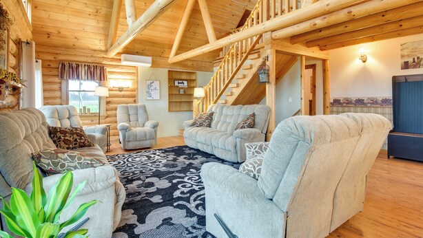 A cozy living room with a large sofa set, a patterned rug, and wooden beams on the ceiling. - Rural New York Vacation Rental w/ Deck (Romulus)