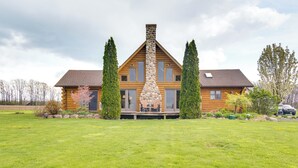A log cabin with a stone chimney, large windows, and a porch with outdoor seating. - Rural New York Vacation Rental w/ Deck (Romulus)