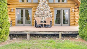 A log cabin with a stone chimney, large windows, and a deck with chairs. - Rural New York Vacation Rental w/ Deck (Romulus)