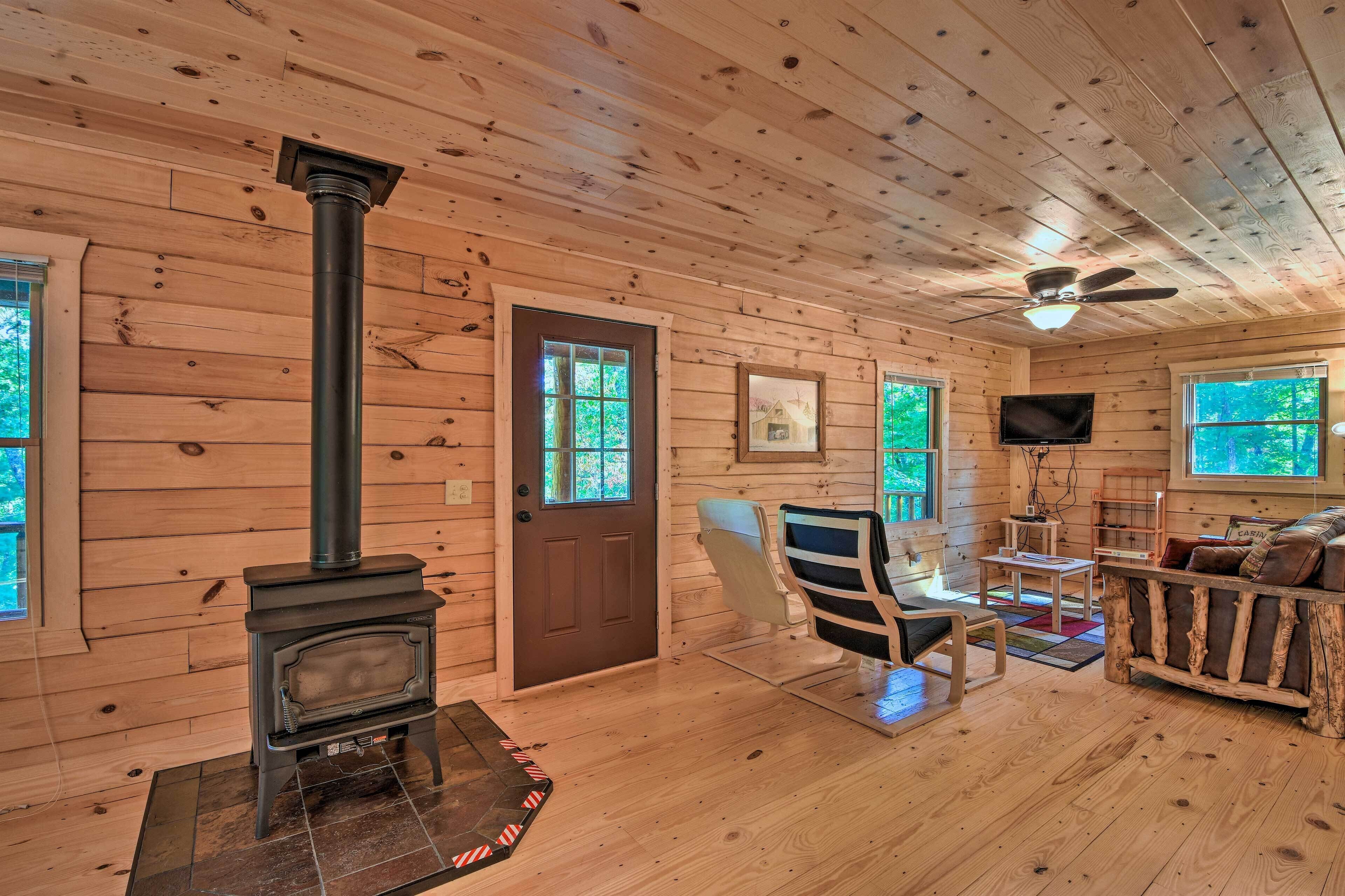 A cozy cabin interior with a wood-burning stove, a ceiling fan, and a fireplace mantel.