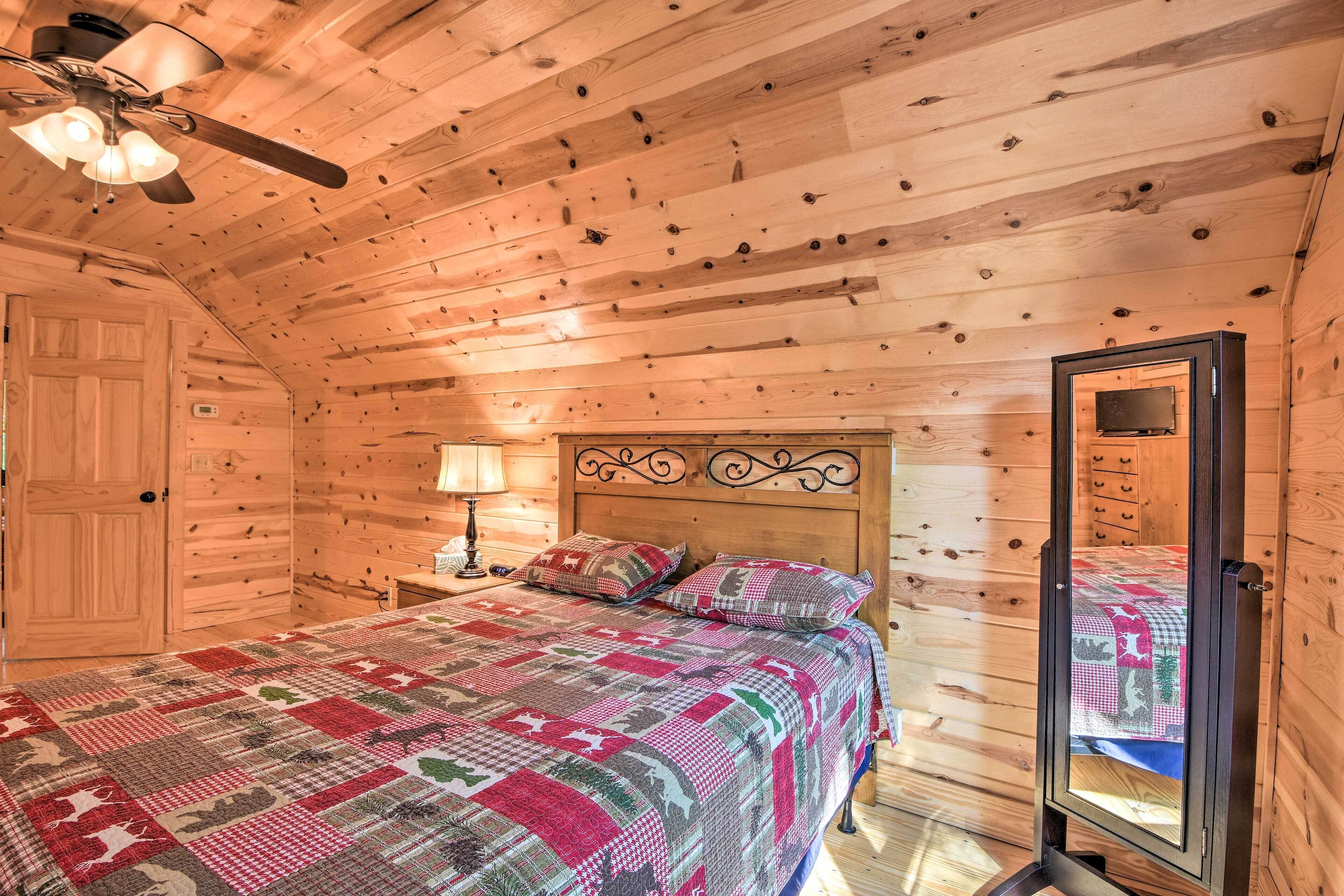 Un dormitorio de cabaña de madera con una cama, una mesita de noche, una lámpara y un ventilador de techo.