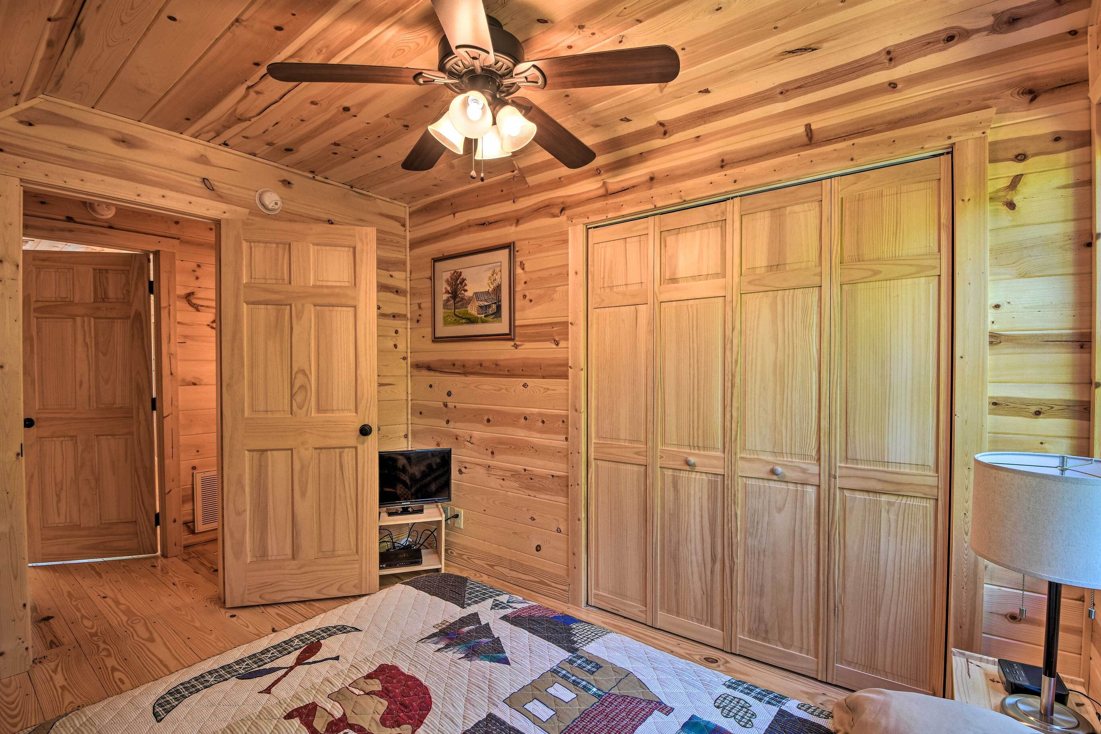Une chambre dans un chalet en bois, équipée d’un lit, d’un ventilateur de plafond, d’une télévision et d’une armoire.