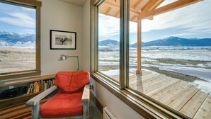 Une pièce dotée d’une grande fenêtre donnant sur un paysage enneigé, d’un fauteuil rouge et d’une bibliothèque.