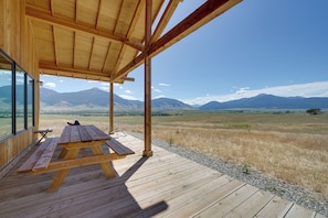 A wooden deck with a picnic table, large windows, and a view of mountains. - Secluded Paradise Valley Retreat w/ Stunning Views (Livingston)