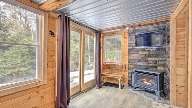 A cozy cabin interior with a stone fireplace, wooden walls, and large windows offering a forest view. - Adirondack Oasis, 15 Mi to Lake George Village! (Chestertown)
