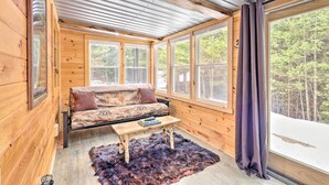 A cozy cabin interior with a wooden interior, a sofa, a table, and large windows offering a view of a forest. - Adirondack Oasis, 15 Mi to Lake George Village! (Chestertown)