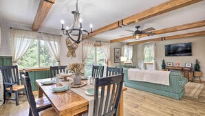 A dining area with a wooden table, chairs, and a chandelier. There is a sofa and a TV in the background. - Adirondack Oasis, 15 Mi to Lake George Village! (Chestertown)