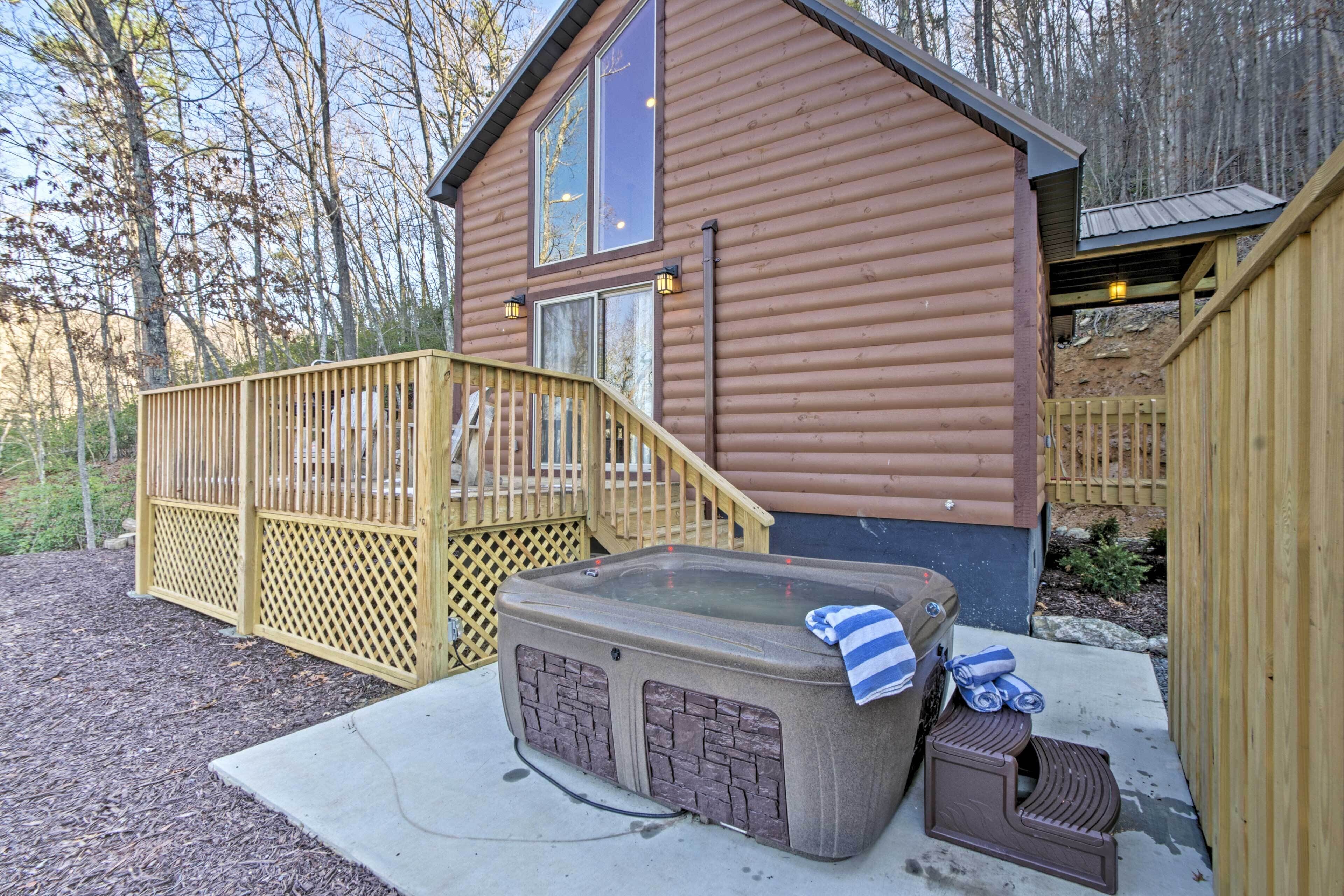 A wooden cabin with a hot tub, a wooden deck, and a staircase leading to the entrance.