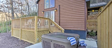 A wooden cabin with a hot tub, a wooden deck, and a staircase leading to the entrance.