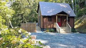A wooden cabin with a red door and a porch, surrounded by gravel and greenery. - Hot Tub & Views: Charming Bryson City Cabin! (Bryson City)