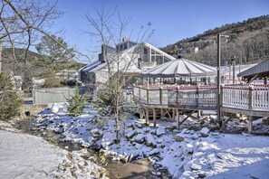 A snow-covered outdoor area with a wooden deck, a small bridge, and a building with a glass facade. - Spacious Family Home w/ Deck at Massanutten Resort (McGaheysville)