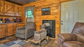 Interior rústico de una cabaña con detalles de madera, una estufa antigua, un sofá de cuero y una zona de cocina con microondas.