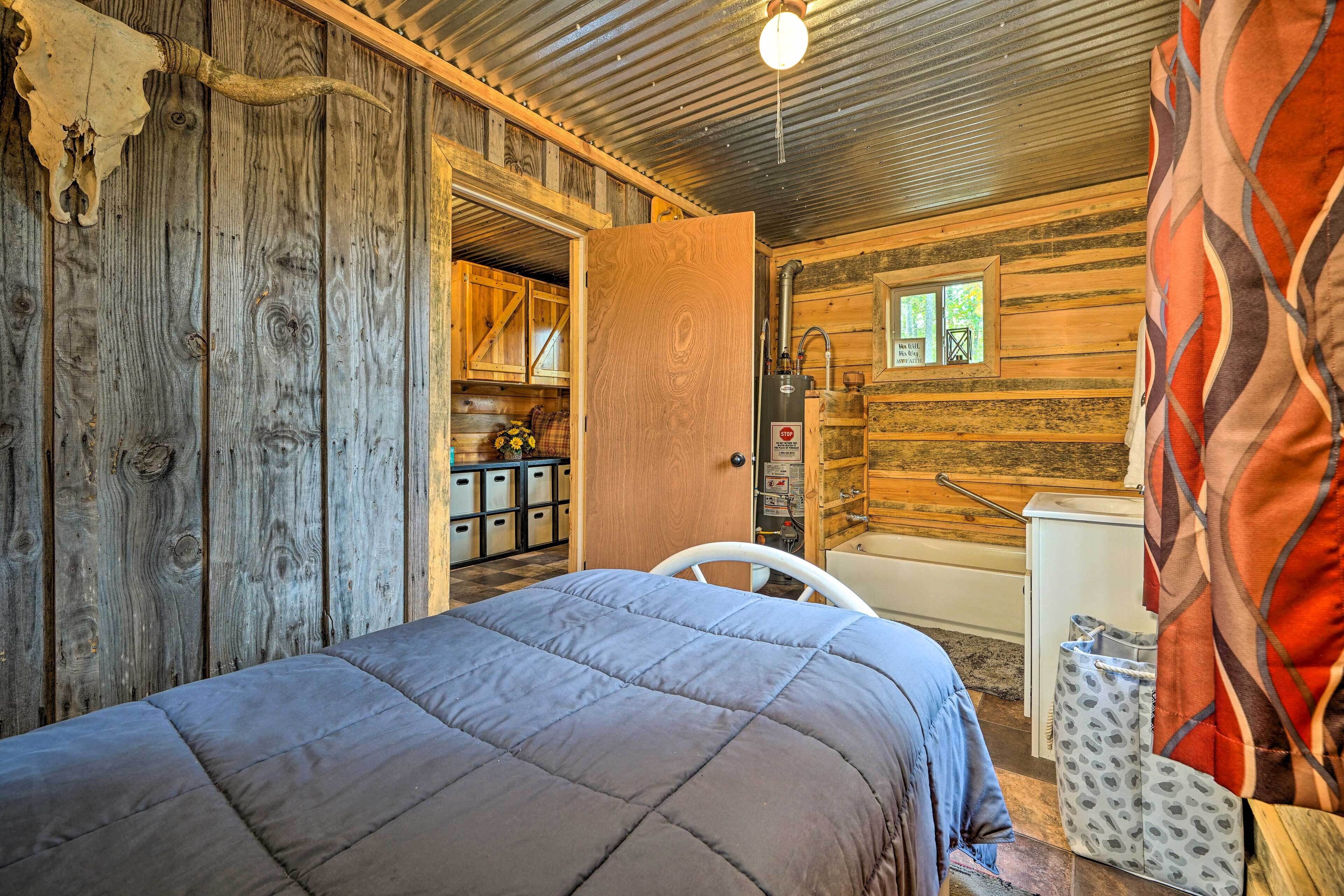 A rustic cabin interior with a bed, wooden walls, a bathroom with a shower, and a window with a view.