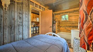 A rustic cabin interior with a bed, wooden walls, a bathroom with a shower, and a window with a view.