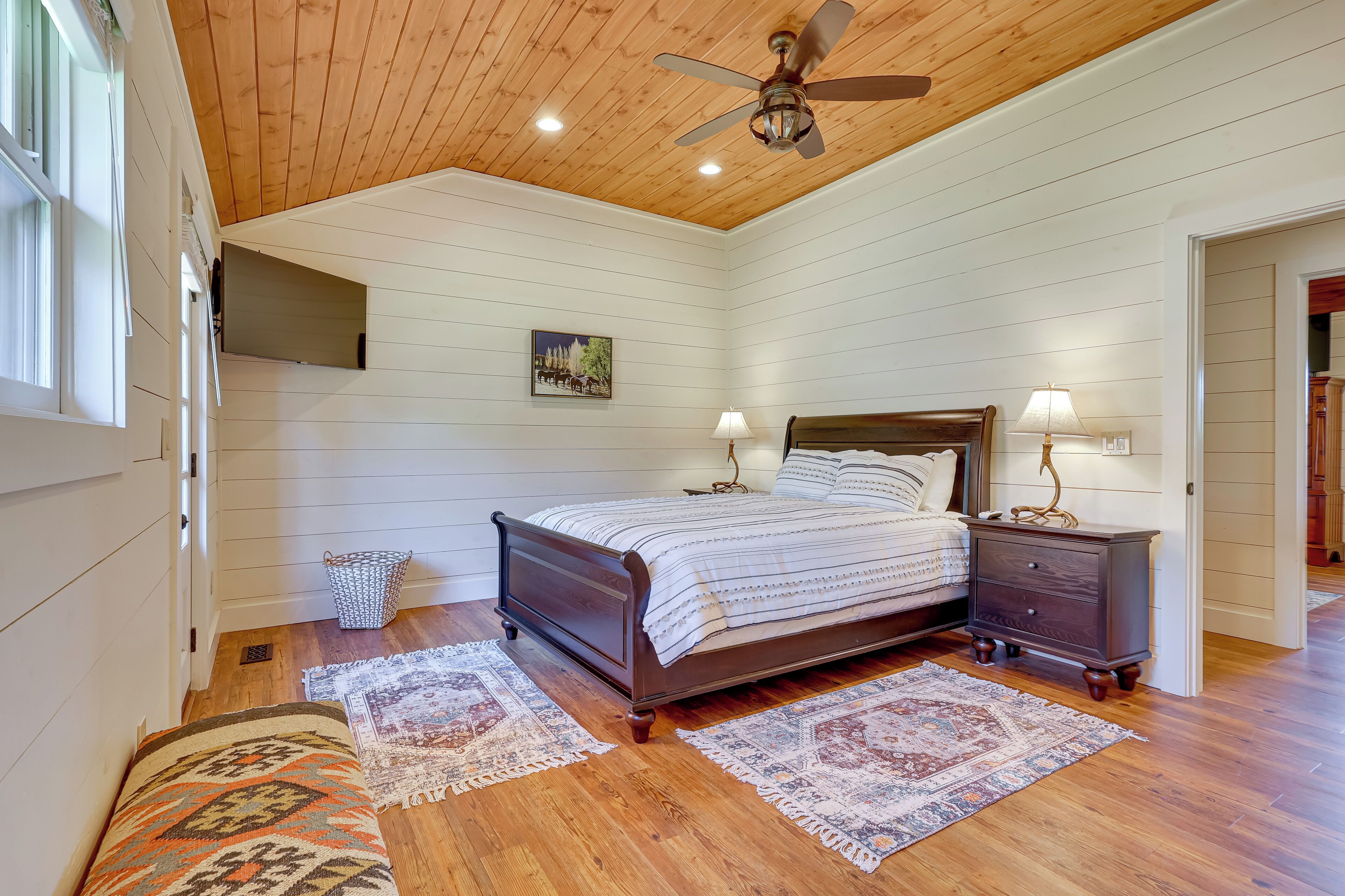 Une chambre avec un plafond en bois, un lit avec une tête de lit, deux tables de chevet avec des lampes et un tapis à motifs sur le sol.