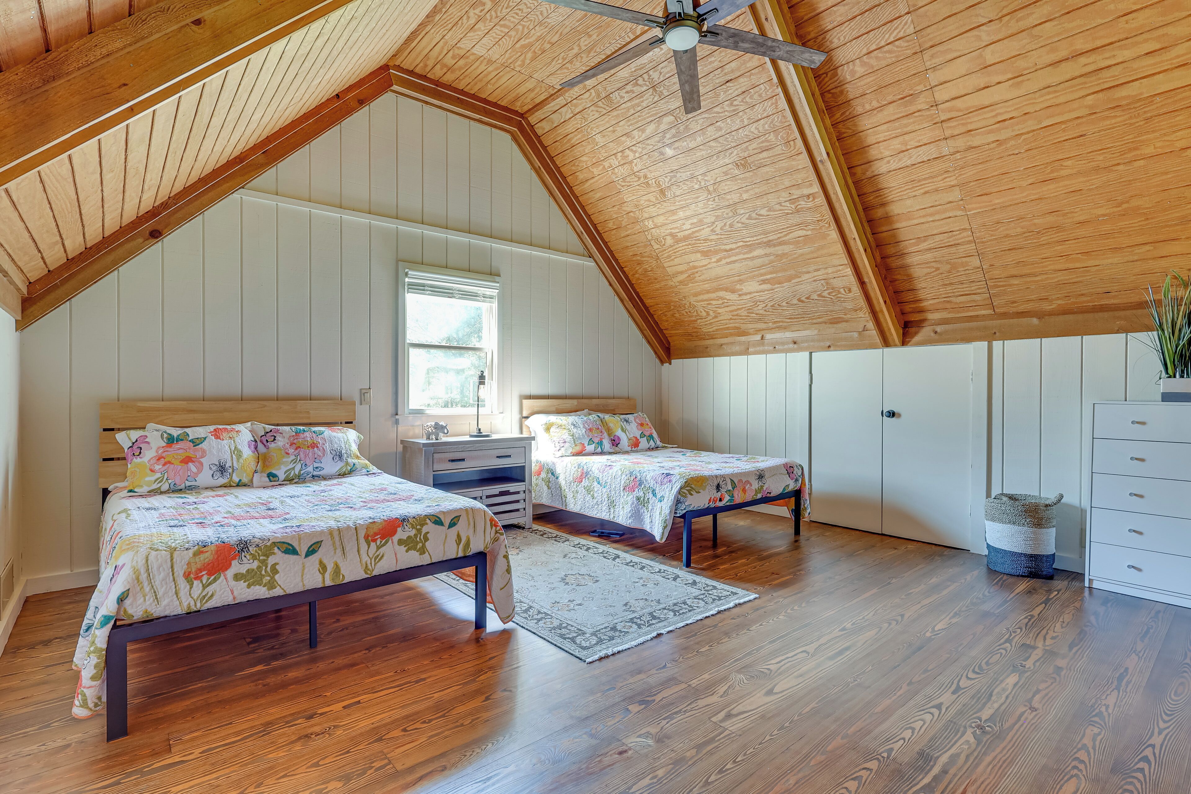 Une chambre avec deux lits, un ventilateur de plafond, un plancher en bois et une fenêtre.