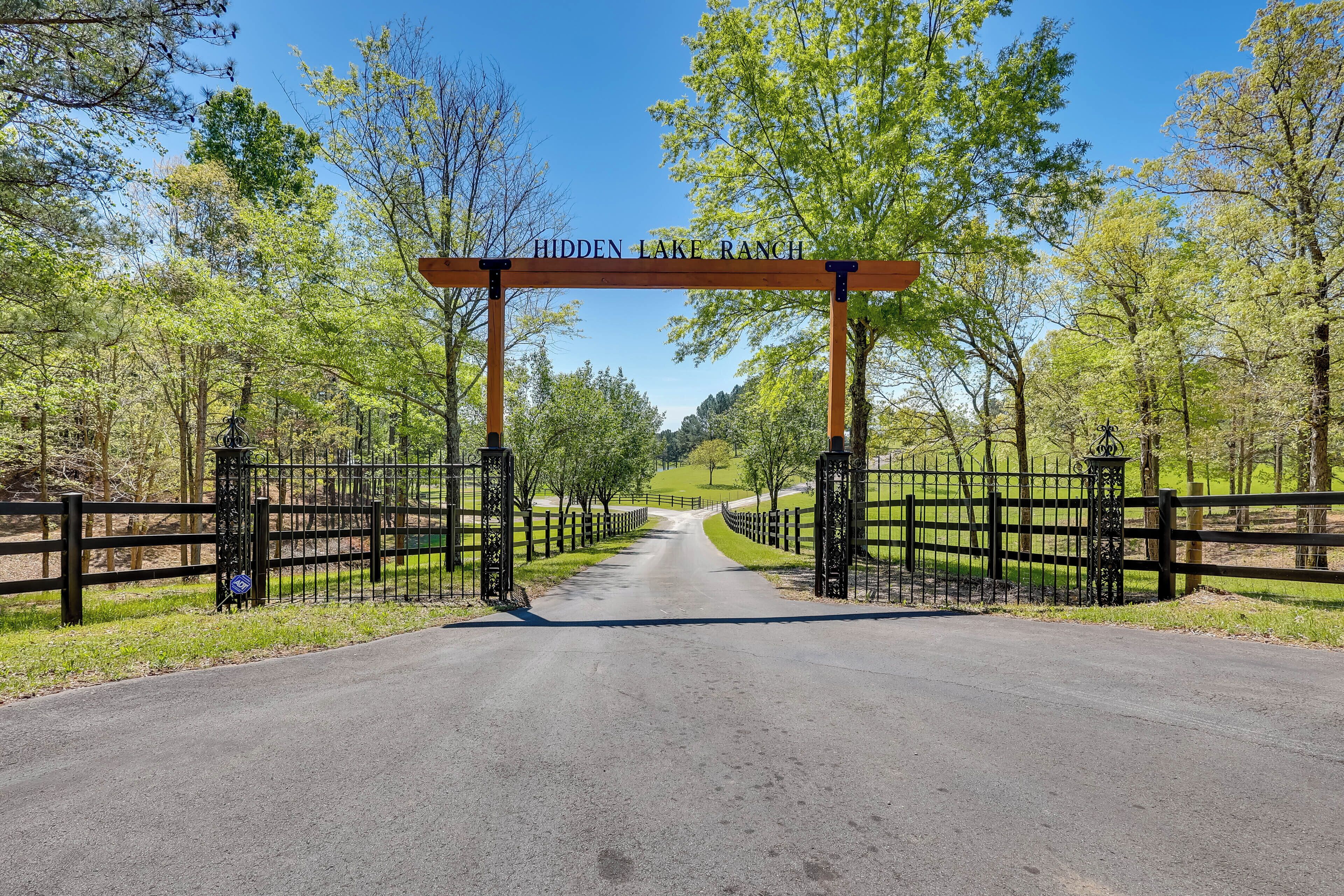 A road leading to Hidden Lake Ranch with a wooden archway and black gates.